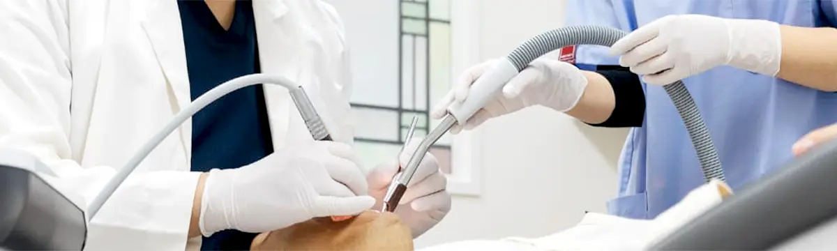 歯科医師と歯科衛生士が患者の口腔内を治療している様子。吸引器や治療器具を用いた診療中の一場面。